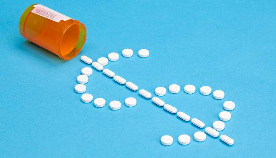 Una botella de pastillas virada sobre un fondo azul y pastillas que forman el signo de dolar