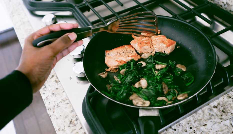 Una mujer cocina salmón, espinaca y setas en una sartén