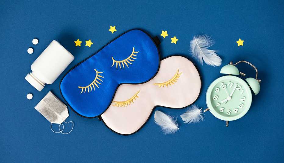 Un pote de pastillas, máscaras para dormir, una bolsa de té, estrellas un reloj despertador y varias plumas sobre un fondo azul