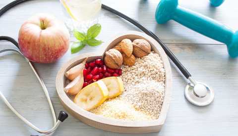 Una manzana, un estetoscopio, unas pesas libres y un plato en forma de corazón con alimentos saludables