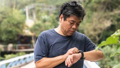 Un hombre mira el conteo de pasos en su reloj inteligente mientras camina por un sendero en el bosque
