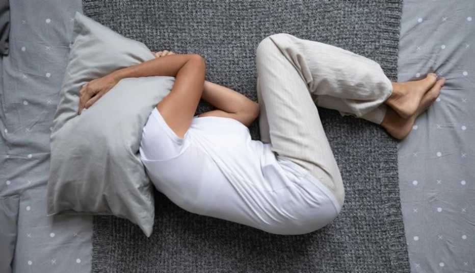Una mujer en su cama, en posición fetal y con la almohada sobre la cabeza, sin poder dormir