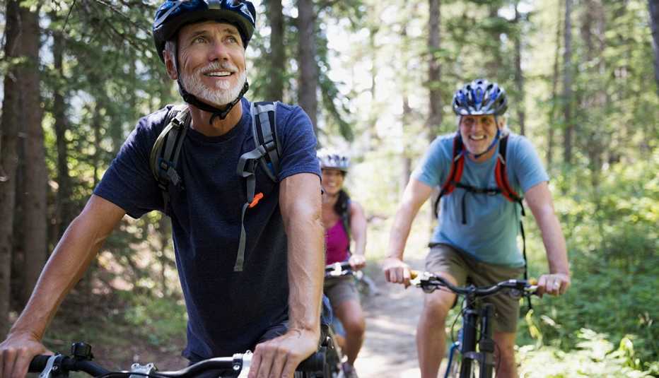 Tres adultos corren bicicleta por un sendero en el bosque
