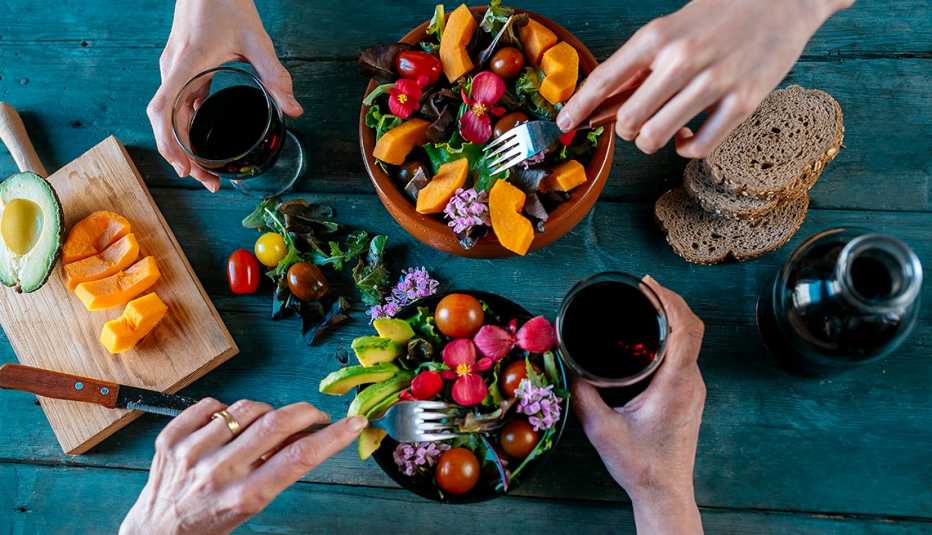 Dos personas cenan ensalada, frutas, pan integral y vino