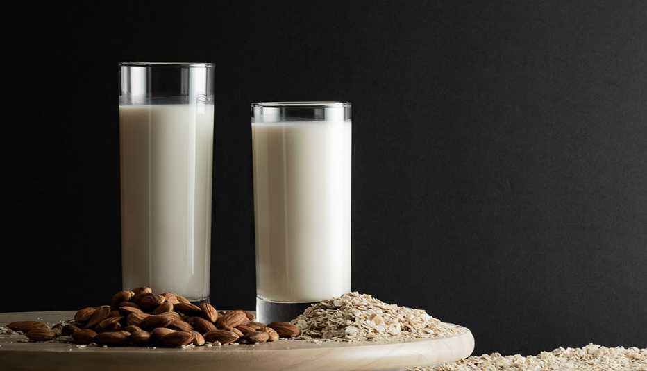 Dos vasos, uno con leche de avena y otro con leche de almendras.