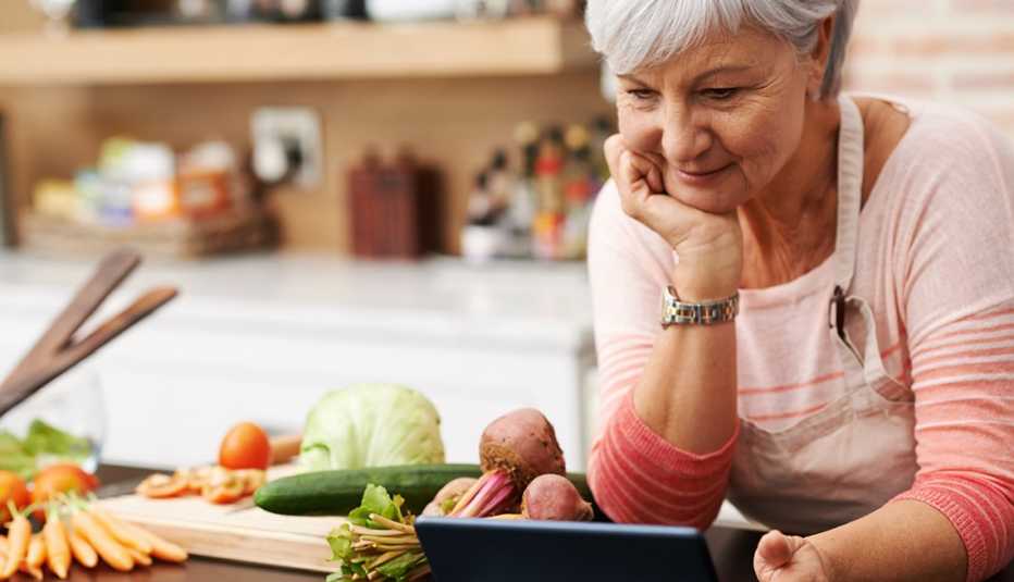 Una mujer en su cocina mira una tableta mientras se prepara para cocinar