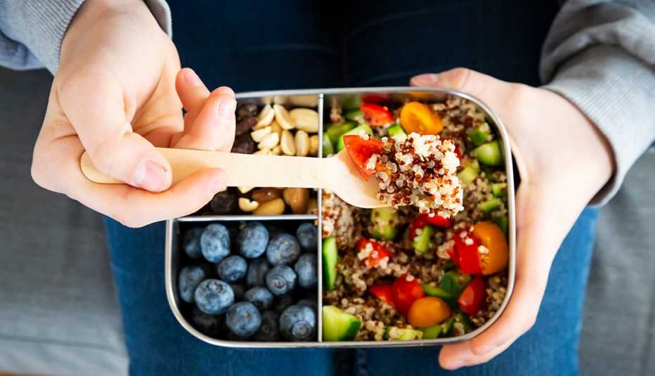 Una persona come su almuerzo que incluye nueces, arándanos y enslada de quinoa