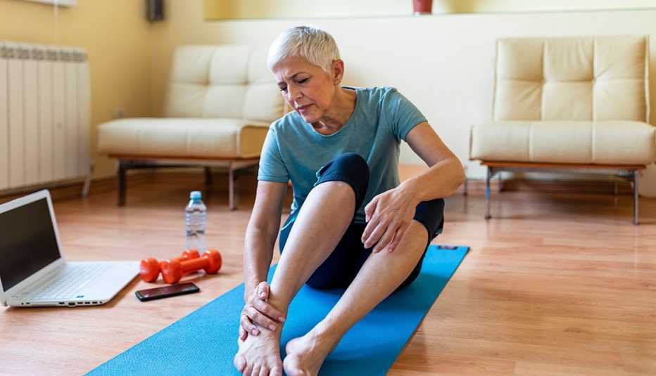 Una mujer sentada en una colchoneta de yoga se masajea el tobillo