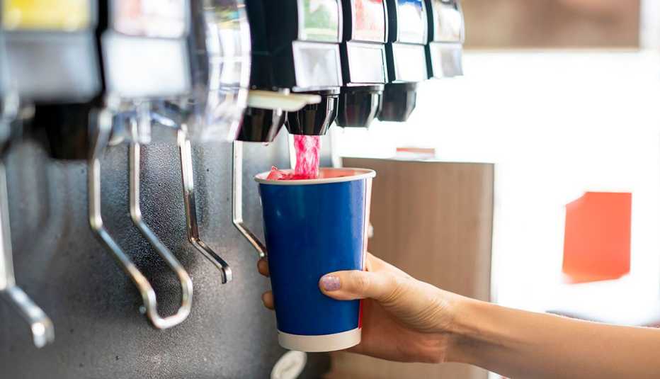 Una persona llena un vaso con soda de una fuente de refrescos
