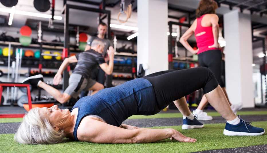Una mujer se ejercita en un gimnasio, al fondo otras personas también hacen ejercicios