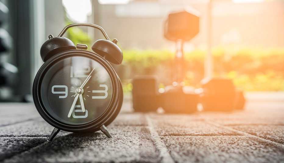 Un reloj despertador en primer plano y al fondo un set de pesas