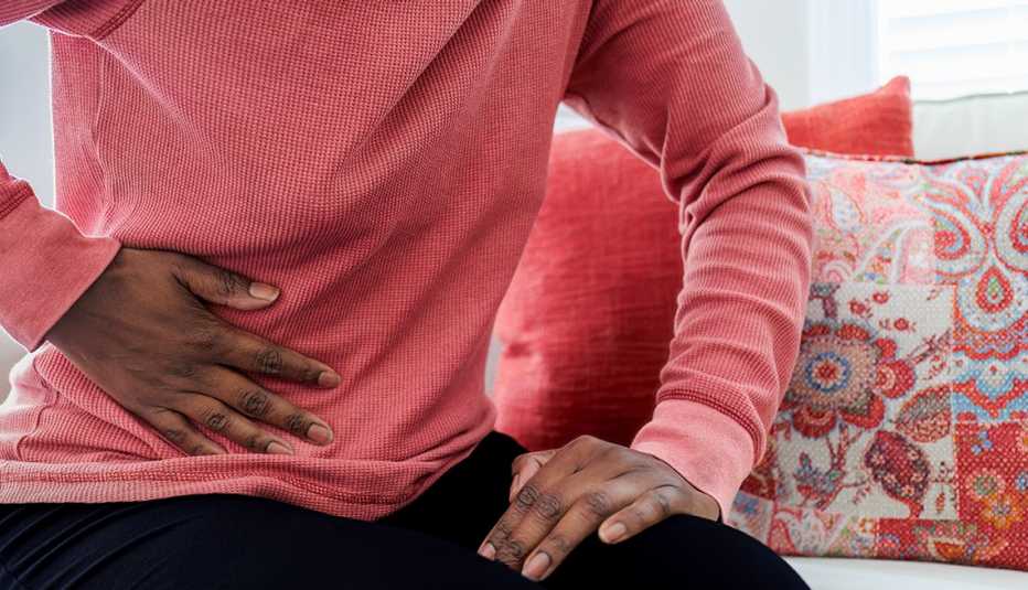 Una mujer sosteniendo su barriga con dolor mientras está sentada en un sofá.