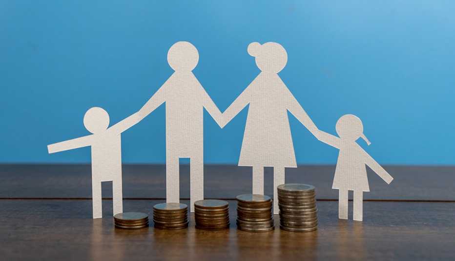 Silueta recortada en papel de una familia tomada de la mano y detrás de monedas apiladas
