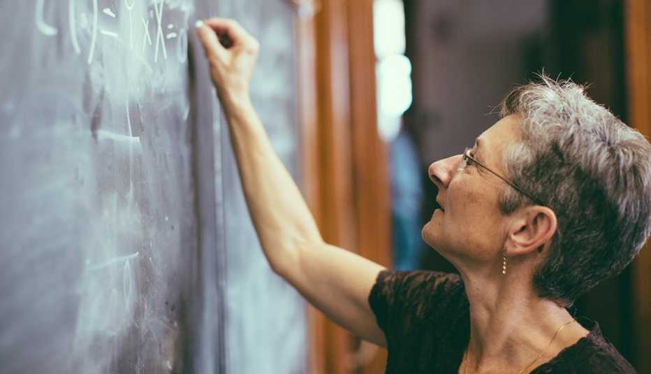 Profesora escribiendo con una tiza en un tablero.
