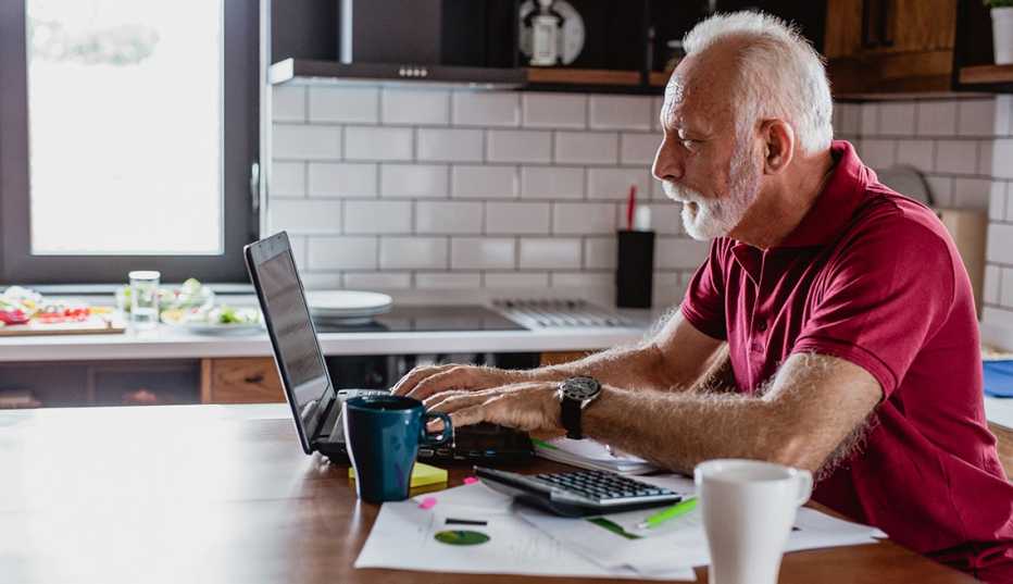 Hombre trabajando en su computadora en la cocina de su casa.