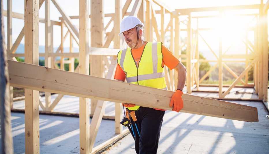 Trabajador de la construcción lleva una viga de madera en una obra