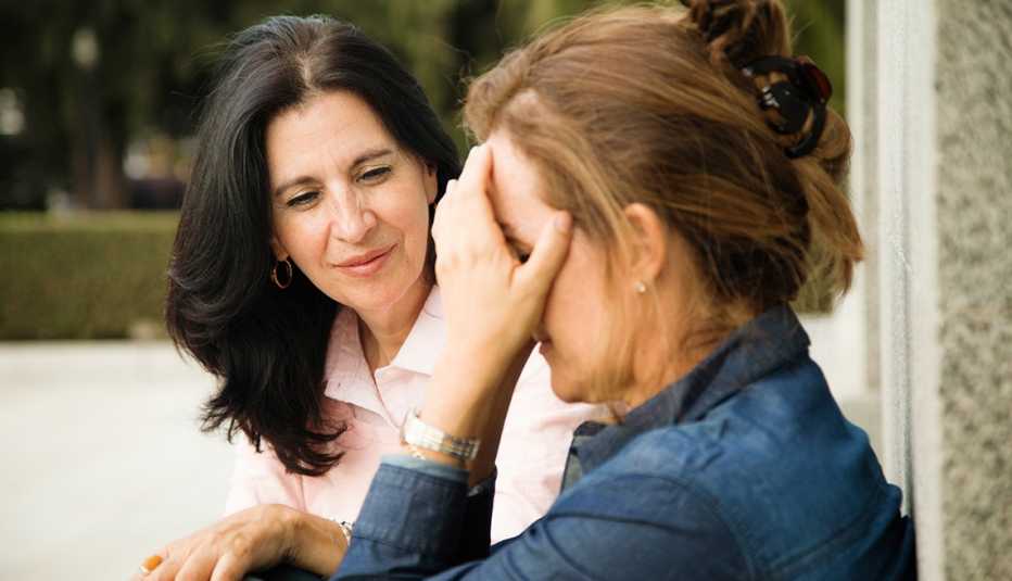 Una mujer consolando a otra que se tapa la cara con sus manos.
