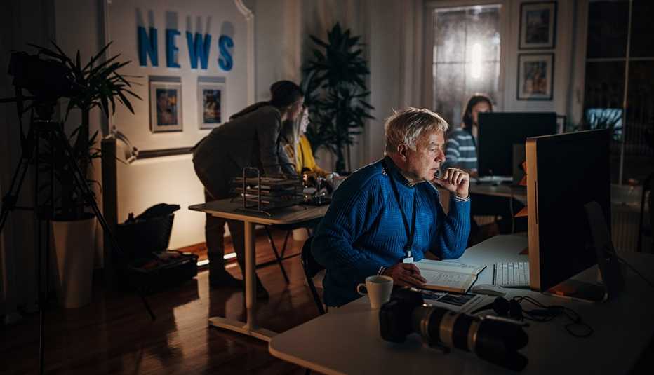 Personas mayores trabajando en varios computadores desde la sala de una casa.