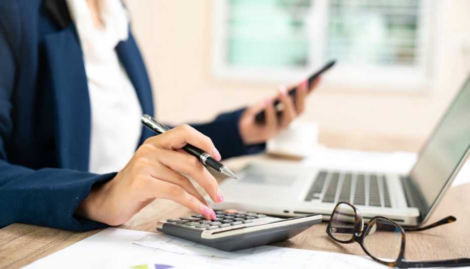Mujer trabajando con una calculadora, un celular en la mano y frente a una computadora.