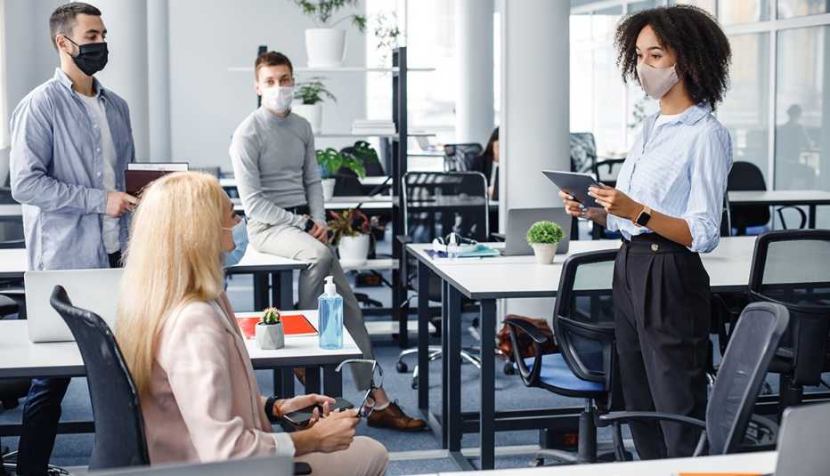 Cuatro personas con mascarilla y con la distancia social de la pandemia en un salón de reuniones.