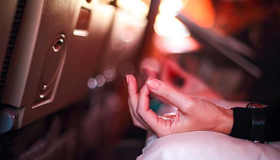 Persona en avión con aerofobia asustada de volar con miedo mientras está sentada en el asiento del avión y haciendo yoga para relajarse.