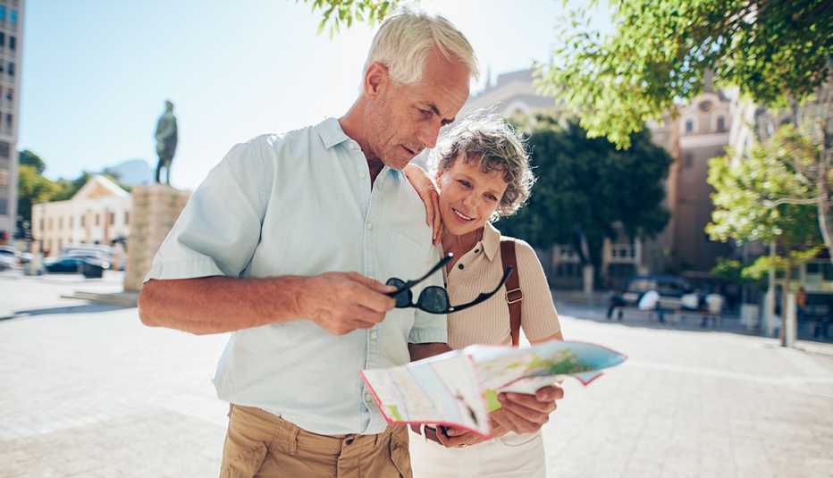 Pareja de adultos mayores observan un mapa mientras están en la calle.