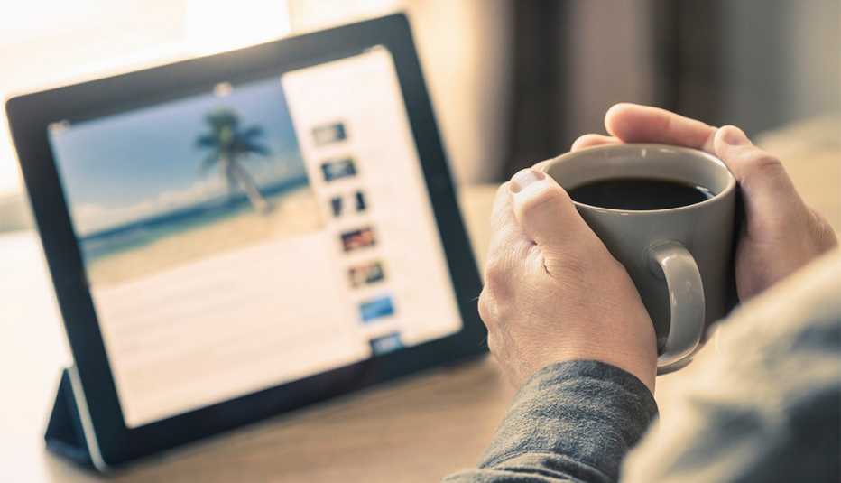 Manos sosteniendo una taza de café con una tableta que muestra una isla tropical