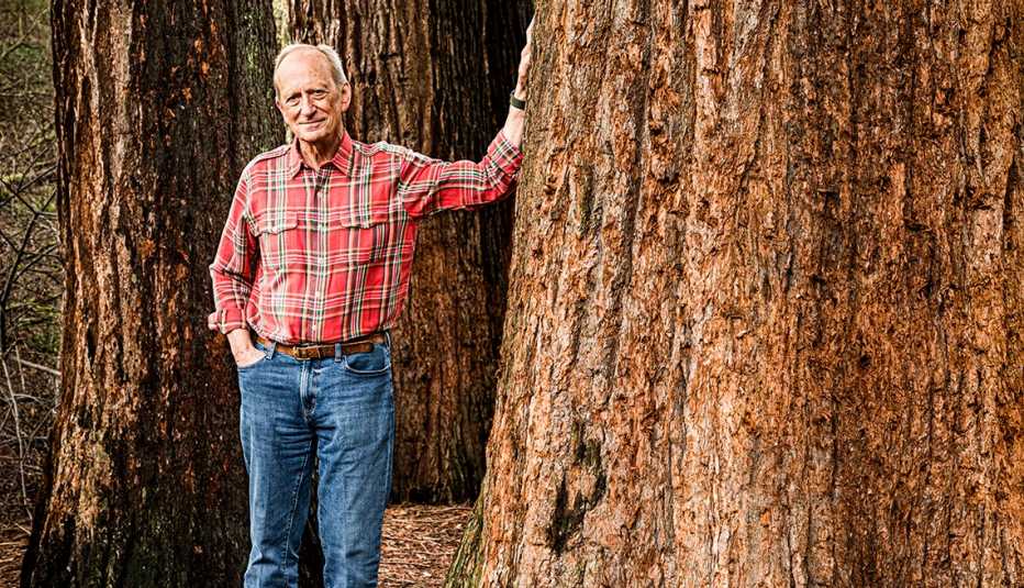 Denis Hayes posa en un bosque con la mano en un gran tronco de árbol