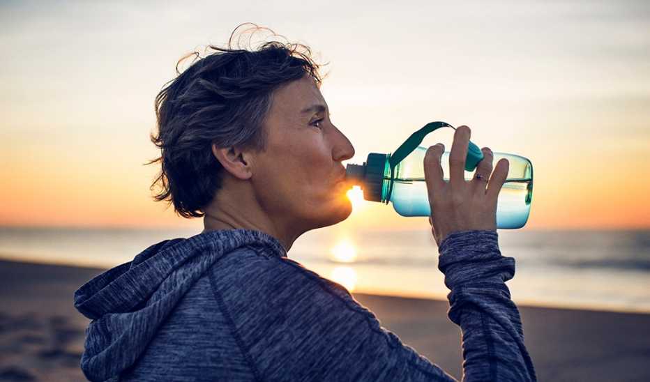 A woman drinking water on a beach at sunset