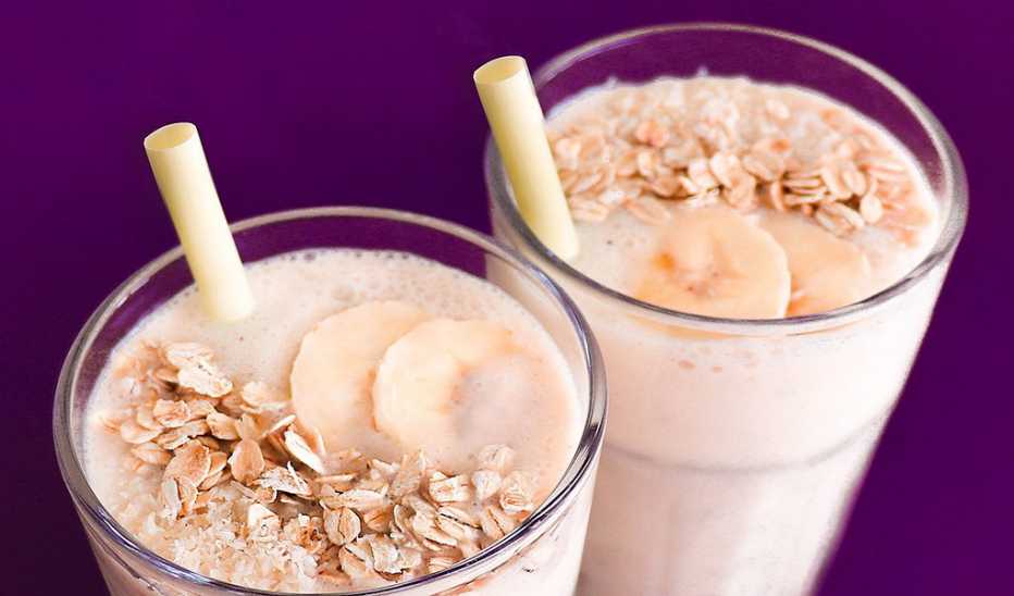 A close-up view of two banana smoothies against a purple background 