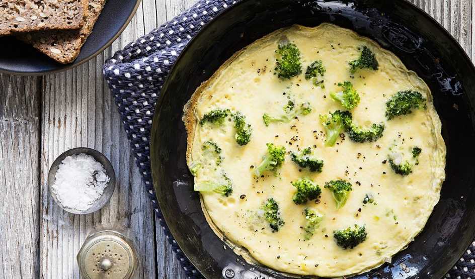 A close-up view of broccoli and parmesan cheese omelet in a pan on a table