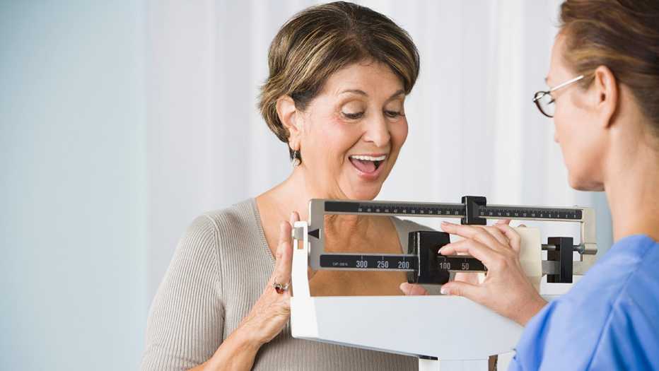 A smiling woman using a medical scale at a doctor's office