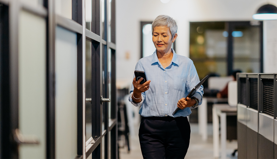 A woman looking at her smartphone while walking in an office